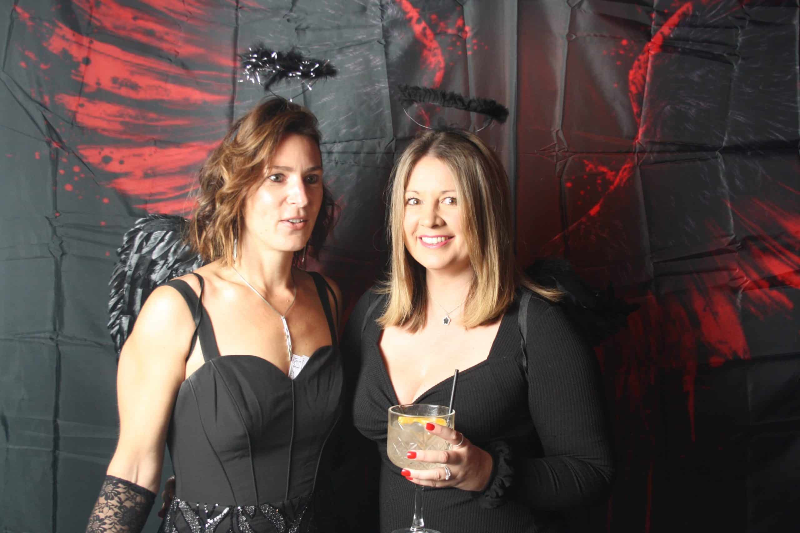 Photobooth 9 Two women in black outfits with spooky wings and halos.